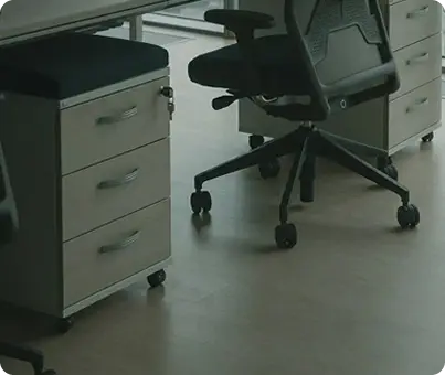 Close-up-of-light-wood-flooring-under-an-office-desk-and-ergonomic-chair.png