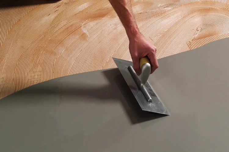 Close-up of a worker using a metal trowel to spread self-levelling compound evenly across a floor before flooring installation