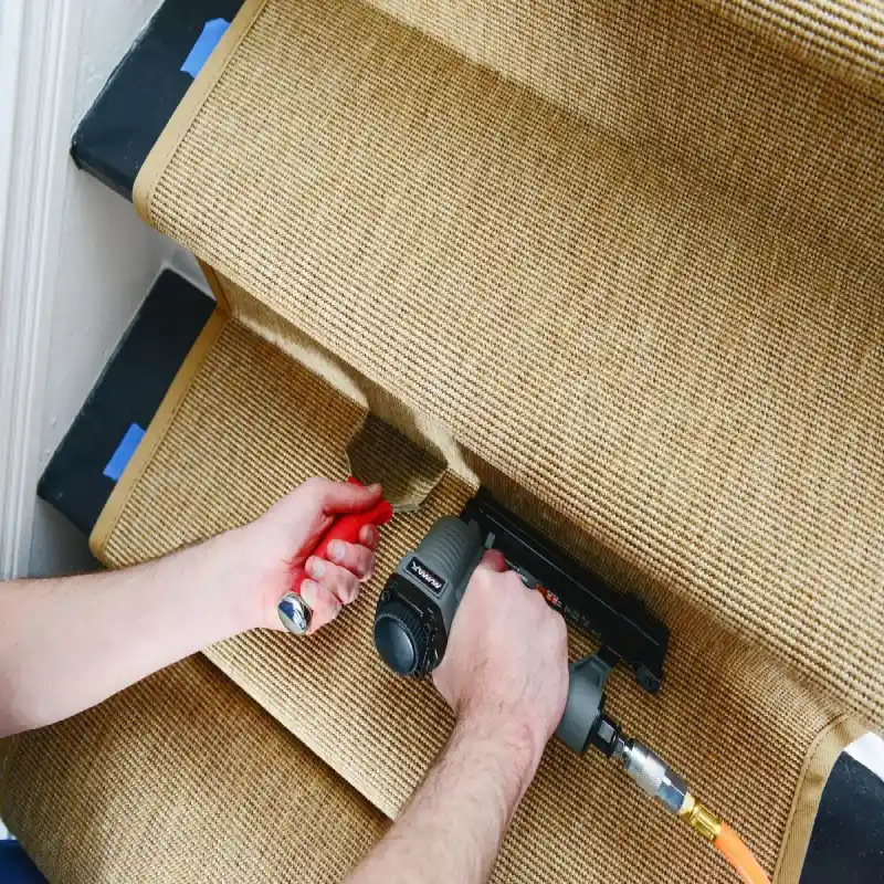 Professional installing textured sisal stair carpet on a staircase, demonstrating sisal stair carpet Dubai installation