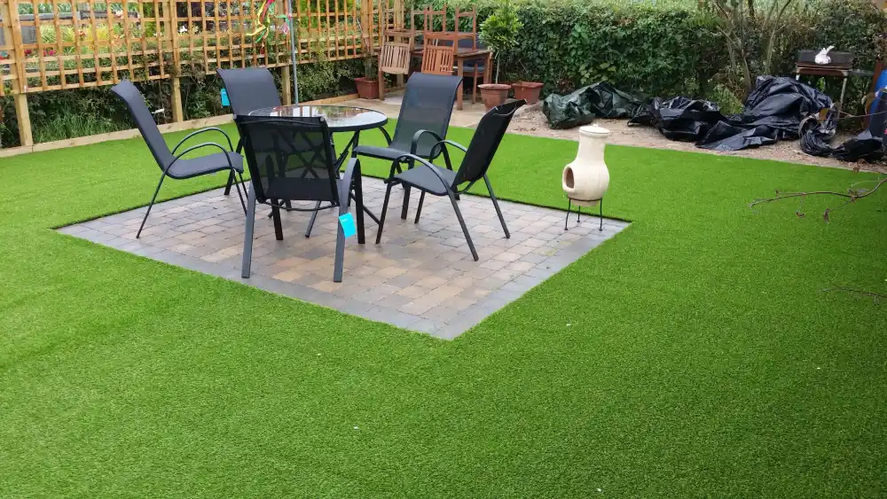 Backyard patio with outdoor dining furniture set on stone pavers surrounded by lush green artificial grass