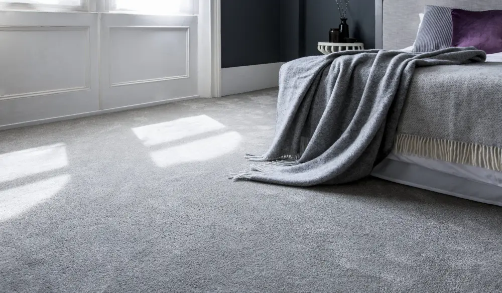 Cozy modern bedroom featuring plush light grey wall-to-wall carpet with a bed and throw blanket