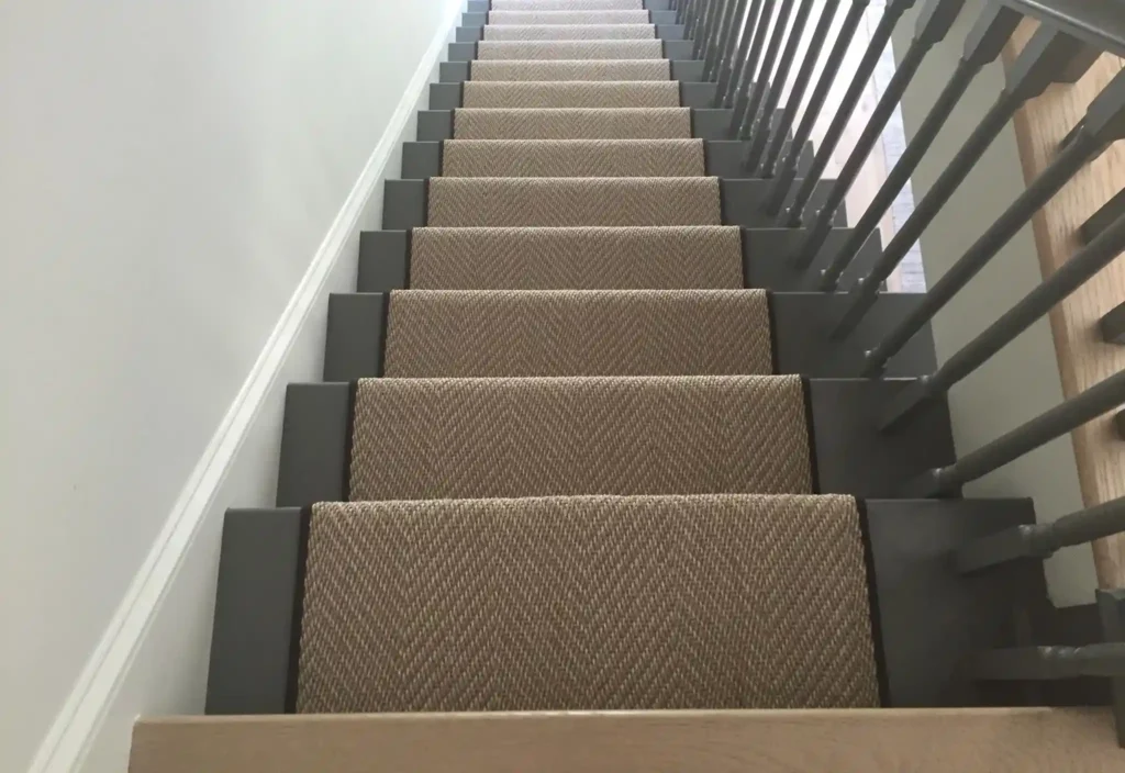 Looking down a painted wooden staircase fitted with a beige textured carpet runner and dark borders
