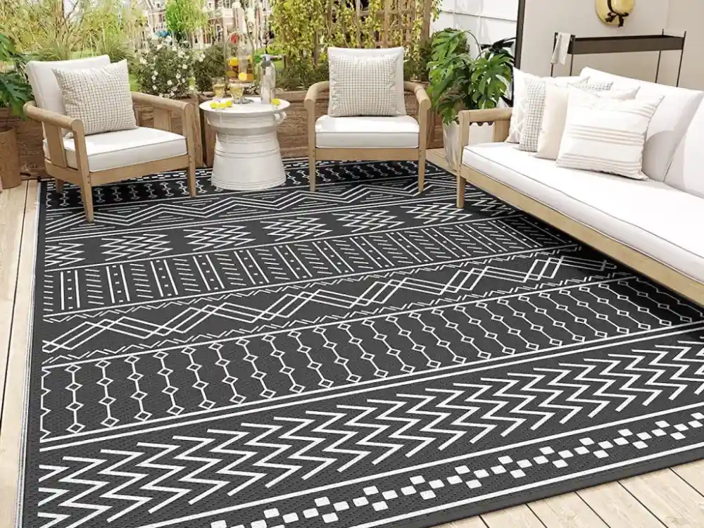 Outdoor patio area furnished with wooden seating and a large black and white geometric pattern area rug